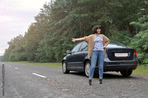 A young woman standing near a broken car with a raised hood is experiencing problems with her vehicle. © Александр Байдук