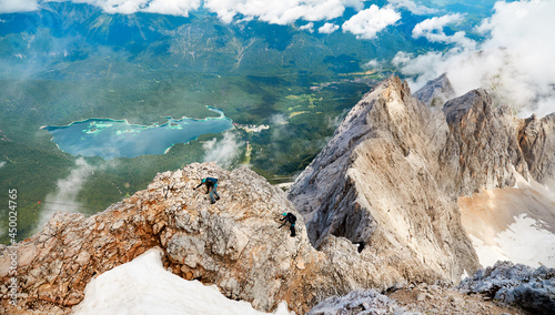 Bergsteiger auf dem Weg zur Zugspitze im Höllental Klettersteig über dem Höllentalferner mit Eibsee im Hintergrund, bewölkter Tag