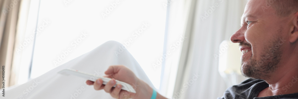 Fototapeta premium Man lying in bed and holding TV remote control at home