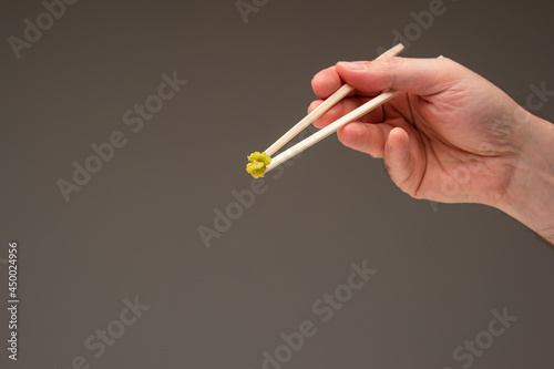 Fototapeta Naklejka Na Ścianę i Meble -  Fresh green Wasabi paste on wooden chopsticks held in hand by Caucasian male hand. Close up studio shot, isolated on gray