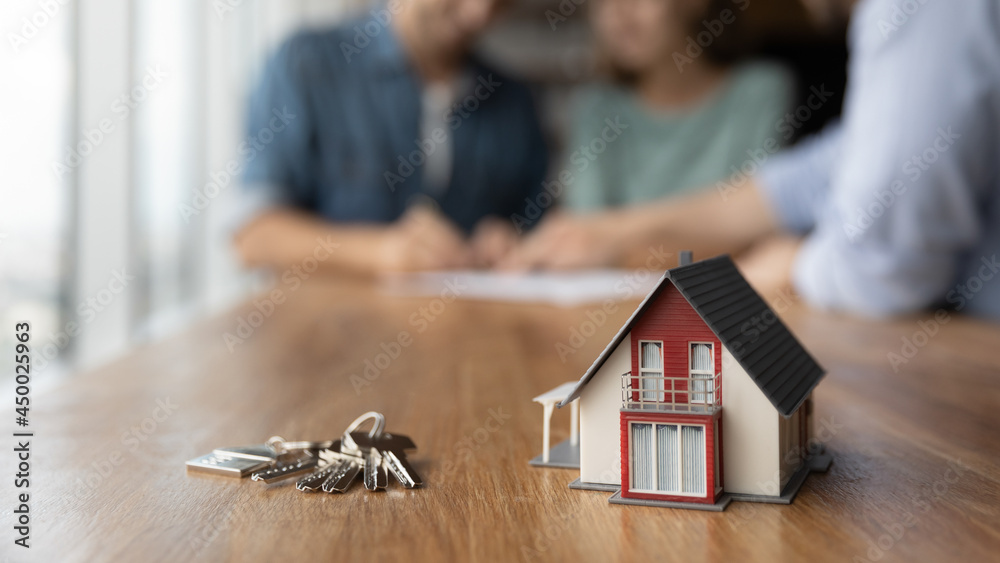 Close up of key and tiny toy house on table. Married couple buying house, consulting, lawyer, legal advisor, real estate agent, bank manager, signing mortgage agreement in background - obrazy, fototapety, plakaty 