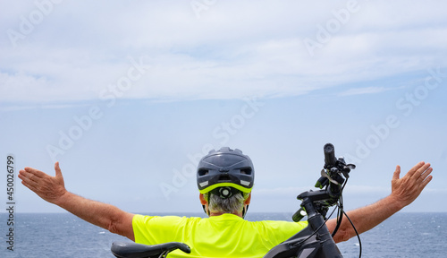 Back view of cyclist man enjoying freedom resting at sea on the cliff after activity with his electro bike.