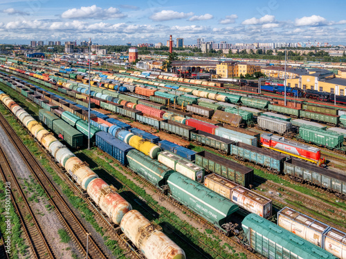 Top view on the railways with various colorful freight wagons. Transportation of various goods by train. Import and export logistics. Industrial landscape. Cargo sorting station. Aerial drone photo.