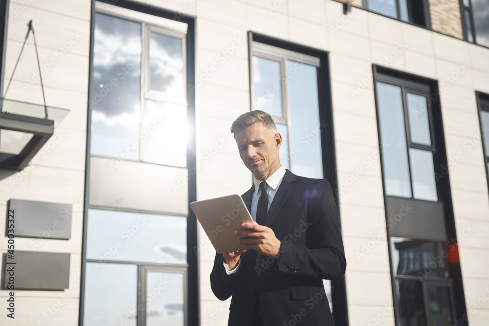 Fototapeta premium Confident mature businessman holding digital tablet while standing near office building