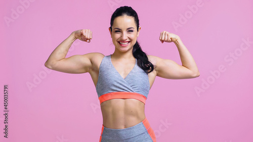 Fototapeta Naklejka Na Ścianę i Meble -  positive sportswoman showing muscles isolated on pink