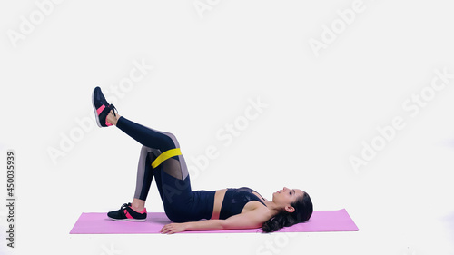 brunette sportswoman working out with yellow elastics on pink fitness mat on white