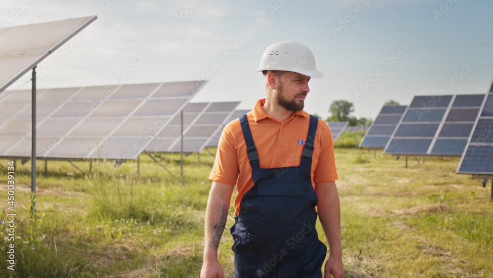 Industrial man engineer in uniform walking through solar panel field for examination. Ecological construction. Solar power station, Green energy concept. Solar station development and energy