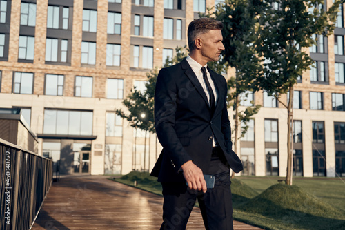 Confident mature businessman walking outdoors with office building on the background