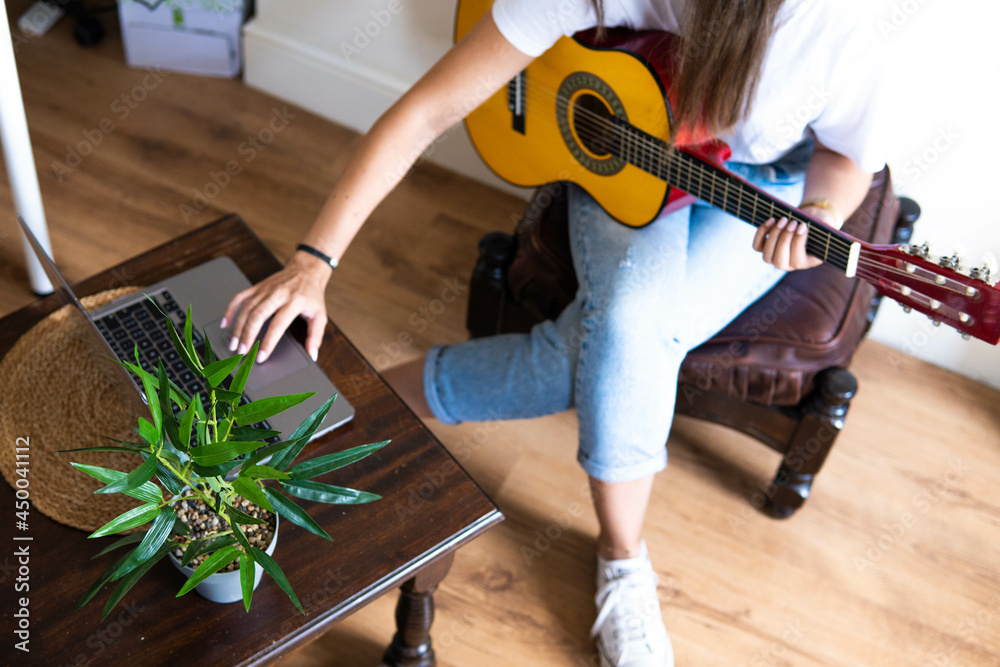 Music Concepts. Latin girl playing guitar. Latin girl learning to play the guitar online. Latin woman checking an online lesson with her computer, relaxing at home