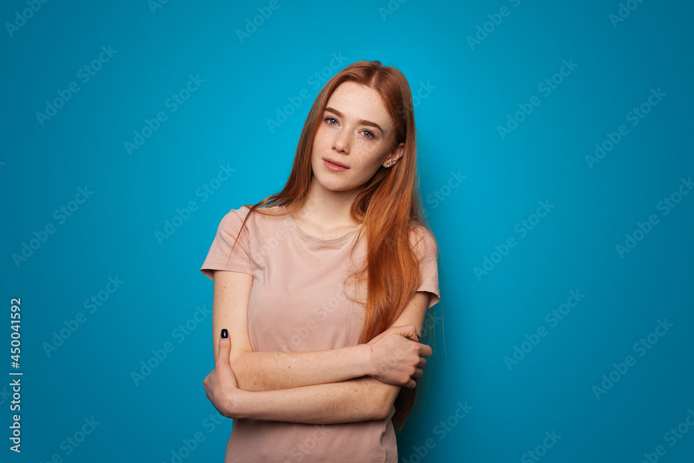 Obraz premium Ginger woman with freckles on a studio wall. Person on blue background. Woman outfit. Fashionable girl smiling.