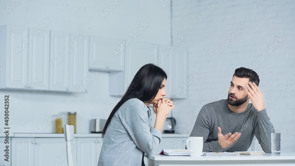 man gesturing while discussing finances with woman in kitchen man gesturing while discussing finances with woman in kitchen