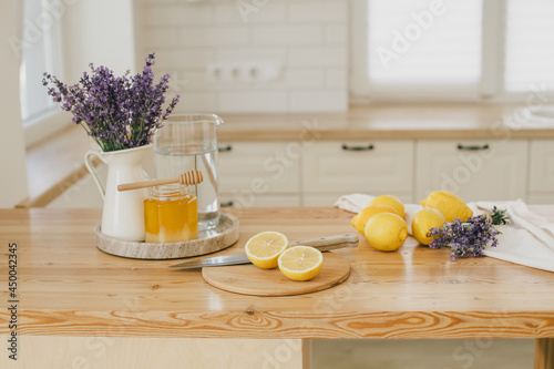 Fresh lemons, jar with honey and bunch of lavender flowers in a vase standing on a kitchen table at home. Ingridients for making lemonade.