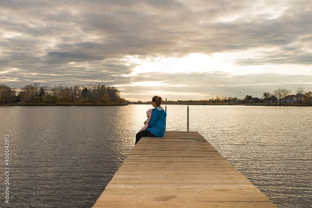 mom and daughter are sitting on the pier at sunset