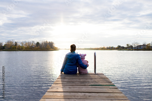 mom and daughter are sitting on the pier at sunset