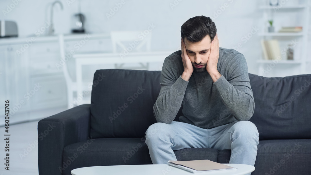 tensed man looking at folder and touching face at home