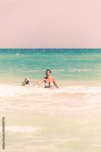 Mom and daughter swim together on the waves, mom teaches daughter to swim