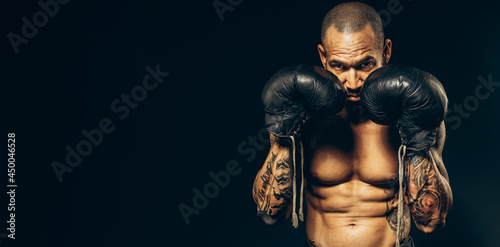 Studio portrait of a muscular boxer in gloves on a dark background. Advertising banner for boxing or martial arts school. A Latino or Cuban with a naked torso in old boxing gloves.