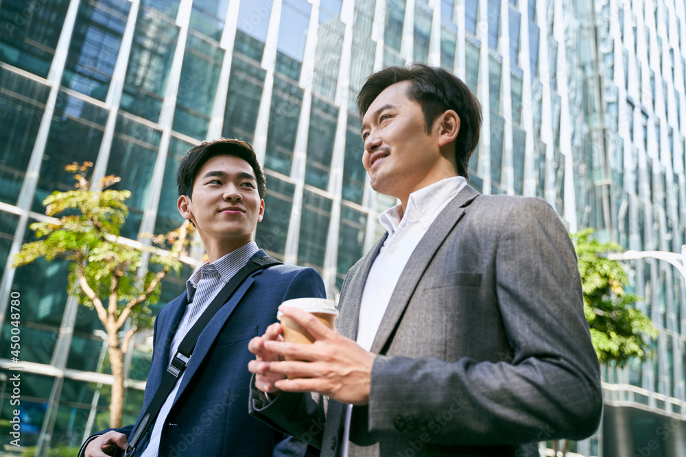 two asian corporate executives discussing business while walking in street two asian corporate executives discussing business while walking in street