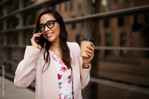 Young businesswoman talking to the phone. Female manager drinking coffee while walking through the city.