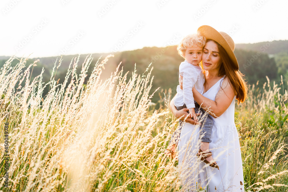 Portrait of a beautiful woman with her son in her arms in a field at sunset. Portrait of a beautiful woman with her son in her arms in a field at sunset.