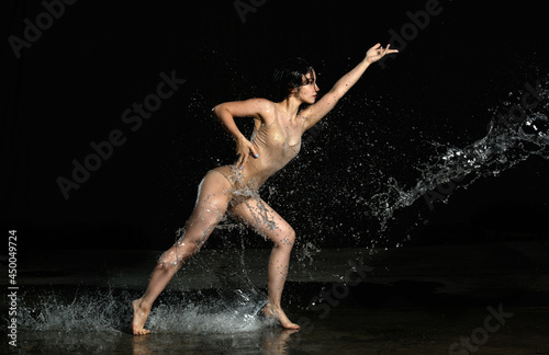 young beautiful woman of Caucasian appearance with long hair dances in drops of water on a black background. Jumping and swinging arms