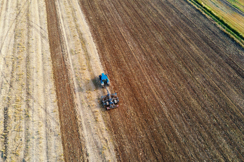 Tractor plows ground on cultivated farm field. Aerial view of tractor preparing the soil for planting crops
