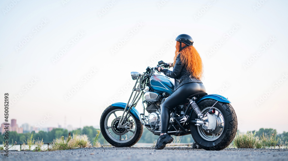 Rear view of red-haired curly woman in helmet on motorcycle outdoors. Rear view of red-haired curly woman in helmet on motorcycle outdoors.