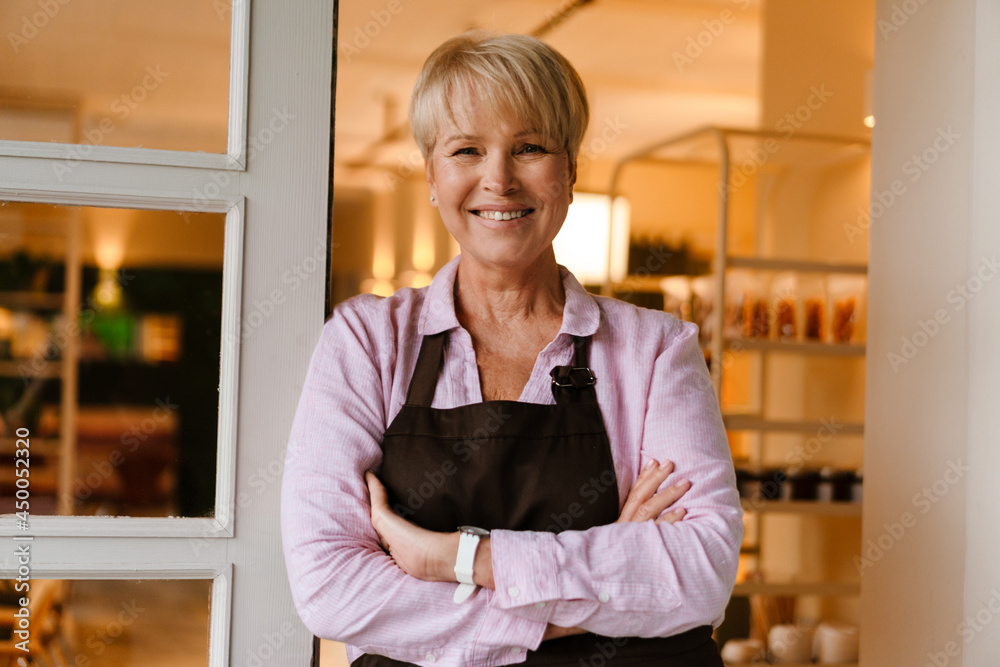 Mature woman smiling at camera while standing in cafe doorway Mature woman smiling at camera while standing in cafe doorway
