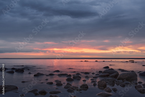 Summer sunset on the Baltic Sea coast during a calm period of twilight with stones in the foreground.