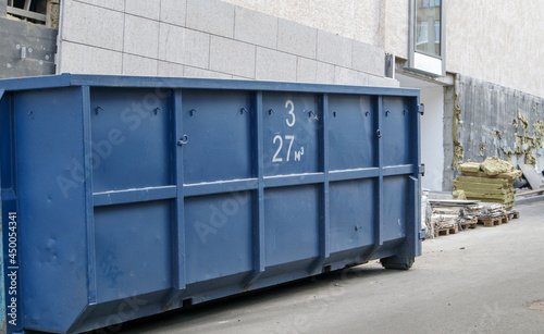 Metal durable blue industrial trash bin for outdoor trash at construction site. Large waste basket for household or industrial waste. A pile of waste.