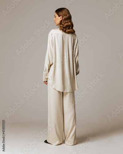 Studio photoshoot of a smiling young brunette woman wearing casual clothing against a brown background.  Natural makeup and wavy hairstyle
