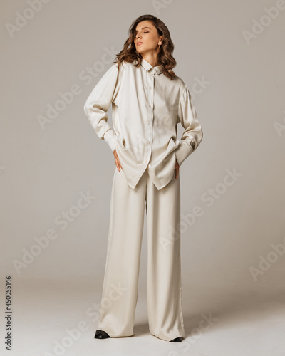Studio photoshoot of a smiling young brunette woman wearing casual clothing against a brown background.  Natural makeup and wavy hairstyle