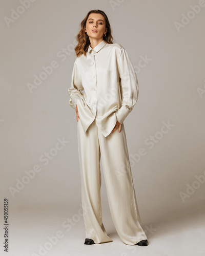 Studio photoshoot of a smiling young brunette woman wearing casual clothing against a brown background.  Natural makeup and wavy hairstyle
