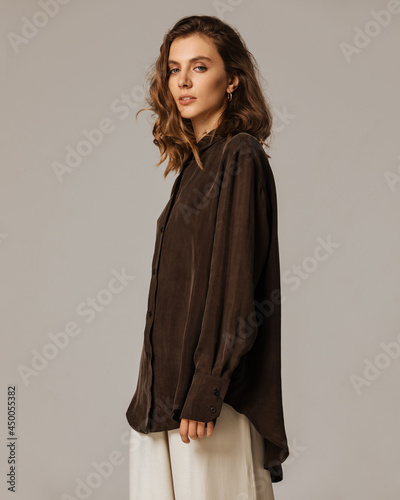 Studio photoshoot of a smiling young brunette woman wearing casual clothing against a brown background.  Natural makeup and wavy hairstyle