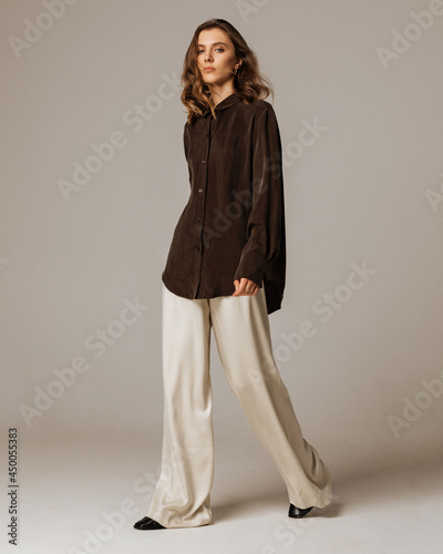 Studio photoshoot of a smiling young brunette woman wearing casual clothing against a brown background.  Natural makeup and wavy hairstyle