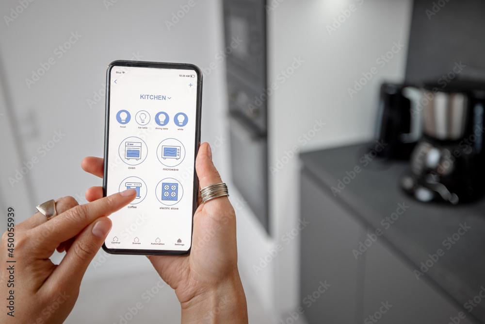 Smart phone with running mobile application to control smart devices in the kitchen. Female controlling smart devices with phone at home. Smart home concept