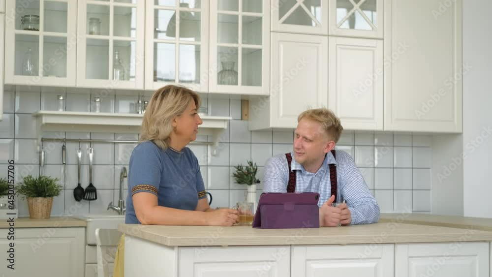 Caucasian Mature Woman with her Grown-up Adult Son Talking while Sitting at Table in the Kitchen. Bonding and Family Reunion, Mothers Day Concept Caucasian Mature Woman with her Grown-up Adult Son Talking while Sitting at Table in the Kitchen. Bonding and Family Reunion, Mothers Day Concept