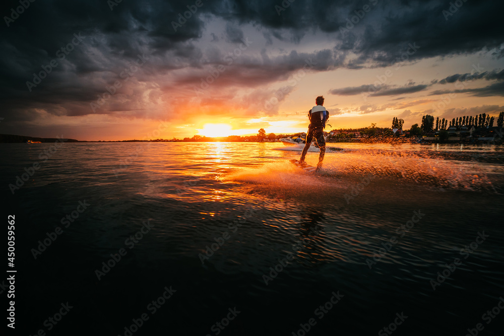 Young man cutting lake surface with wake board