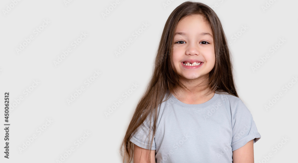 Portrait of a beautiful happy laughing child girl, close-up. Happy childhood concept, smiling. Little girl in white or grey blank t-shirts. The tooth is growing in the wrong place. Portrait of a beautiful happy laughing child girl, close-up. Happy childhood concept, smiling. Little girl in white or grey blank t-shirts. The tooth is growing in the wrong place.