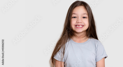 Portrait of a beautiful happy laughing child girl, close-up. Happy childhood concept, smiling. Little girl in white or grey blank t-shirts. The tooth is growing in the wrong place.