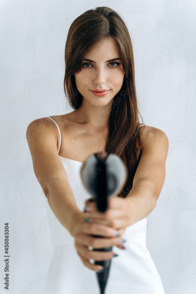 At gunpoint. Beautiful happy woman drying healthy long straight hair using hair dryer. Portrait of attractive girl with brunette hair holding hairdryer like a gun. Hairstyle and hairdressing concept At gunpoint. Beautiful happy woman drying healthy long straight hair using hair dryer. Portrait of attractive girl with brunette hair holding hairdryer like a gun. Hairstyle and hairdressing concept