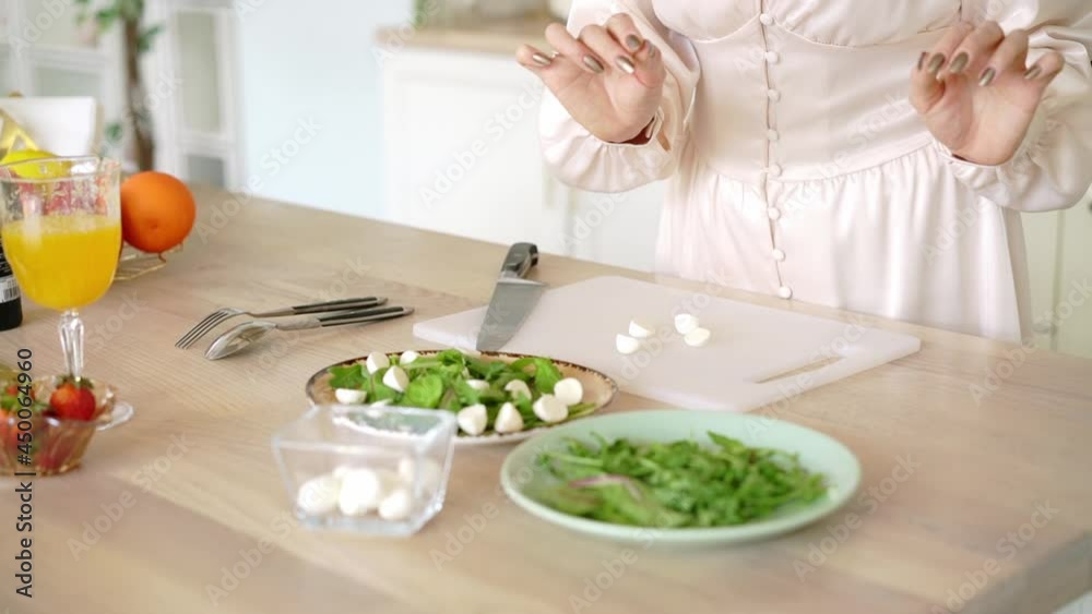 A young woman makes a fruit and vegetable salad with arugula and strawberries. Girl cooking diet salad in the kitchen. High quality FullHD footage A young woman makes a fruit and vegetable salad with arugula and strawberries. Girl cooking diet salad in the kitchen. High quality FullHD footage