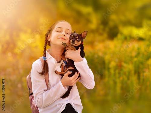 Adorable smiling little girl child schoolgirl holding and playing with pet dog. Friends.