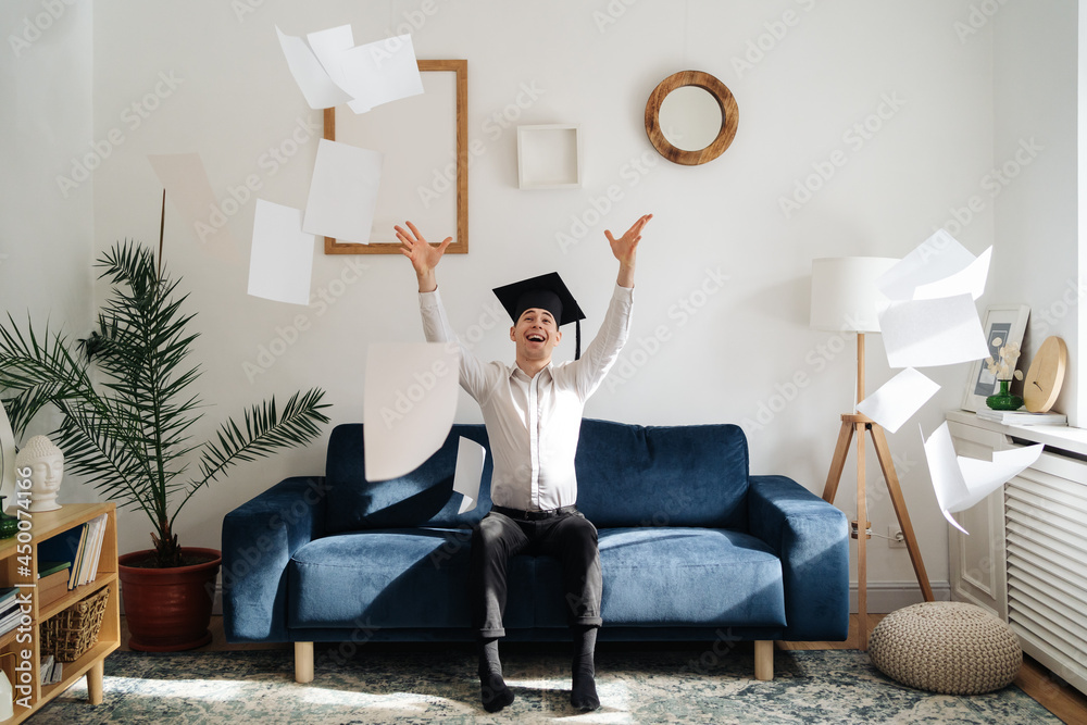 Education, graduation and people concept - top view of happy male student throwing a bunch of sheets at home showing his emotions