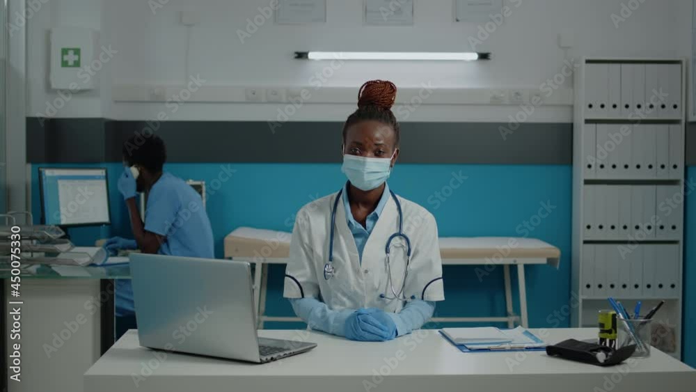 Close up of woman working as doctor in medical cabinet at facility. Portrait of young medic wearing face mask and sitting at desk with laptop, documents, files, and checkup papers Close up of woman working as doctor in medical cabinet at facility. Portrait of young medic wearing face mask and sitting at desk with laptop, documents, files, and checkup papers