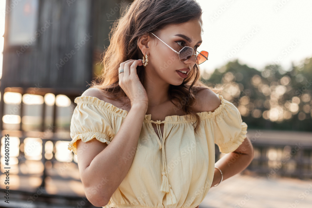 Stylish attractive girl in fashion sunglasses in a summer yellow outfit stands near the lake in nature. Stylish attractive girl in fashion sunglasses in a summer yellow outfit stands near the lake in nature.