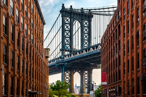 Fototapeta Naklejka Na Ścianę i Meble -  Manhattan Bridge between Manhattan and Brooklyn over East River seen from a narrow alley enclosed by two brick buildings on a sunny day in Washington street in Dumbo, Brooklyn, NYC