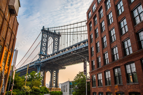 Manhattan Bridge between Manhattan and Brooklyn over East River seen from a narrow alley enclosed by two brick buildings on a sunny day in Washington street in Dumbo, Brooklyn, NYC © Stefan