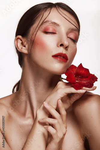 Pretty woman with red flower in her hands near the face naked shoulders clear skin model with pink makeup. Skin care and Spa concept on white background. Woman looking at camera