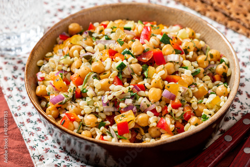 Salad of bulgur, chickpeas and vegetables in a bowl close-up. Salad with chickpea, bulgur, tomato, pepper, cucumber, onion, parsley, and lemon juice. Vegan food, Middle Eastern food.
